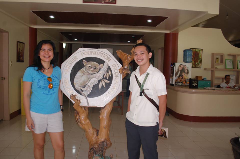 PTFI program manager and HNU Student researcher pose with the PTFI logo inside the Tarsier Info Center